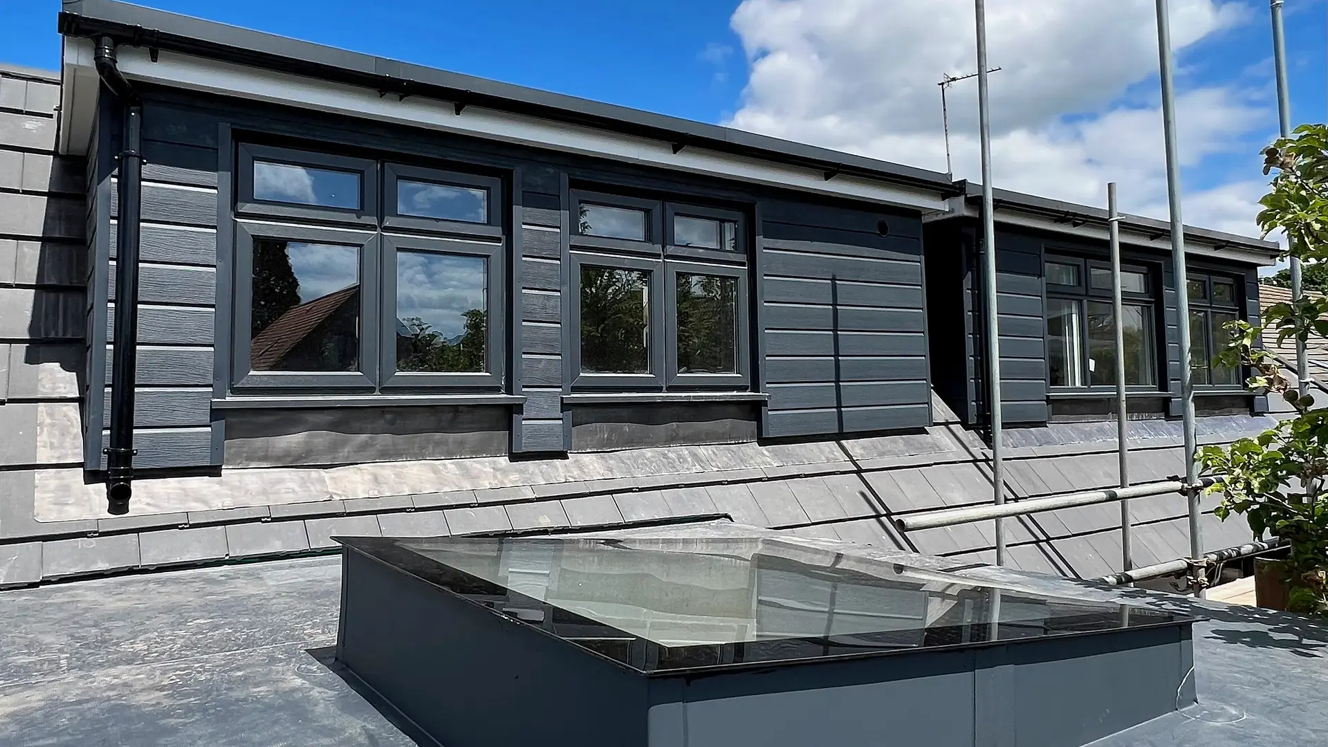 Wide flat-roof dormer loft conversion clad in dark grey, with new windows and a roof lantern below