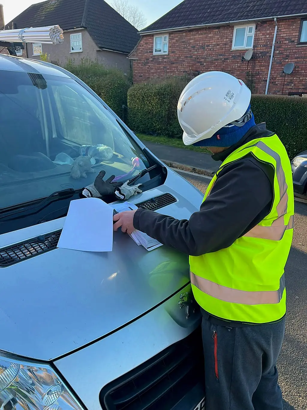 Site manager in a white hard hat reviewing plans outside a Bristol semi